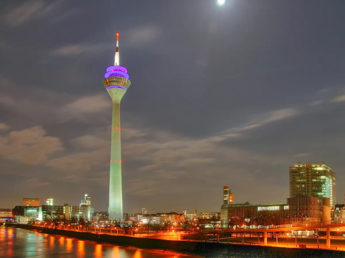 Düsseldorf: ein schlanker Fernsehturm aus Beton am Rheinufer neben moderner Uferbebauung