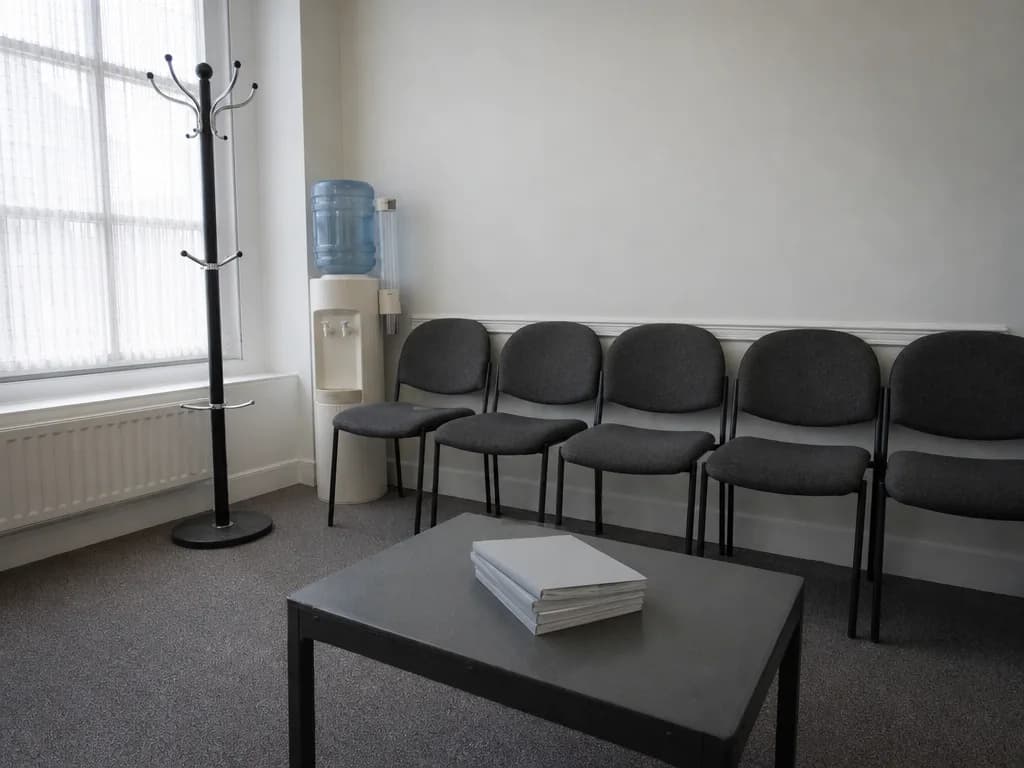 Ein leeres Wartezimmer mit gepolsterten Stühlen und Tageslicht durch ein Fenster