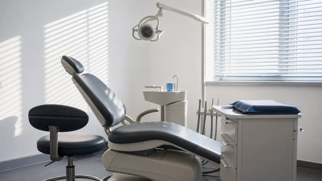 Ein leeres Behandlungszimmer mit Arbeitshocker und Tageslicht durch eine Jalousie