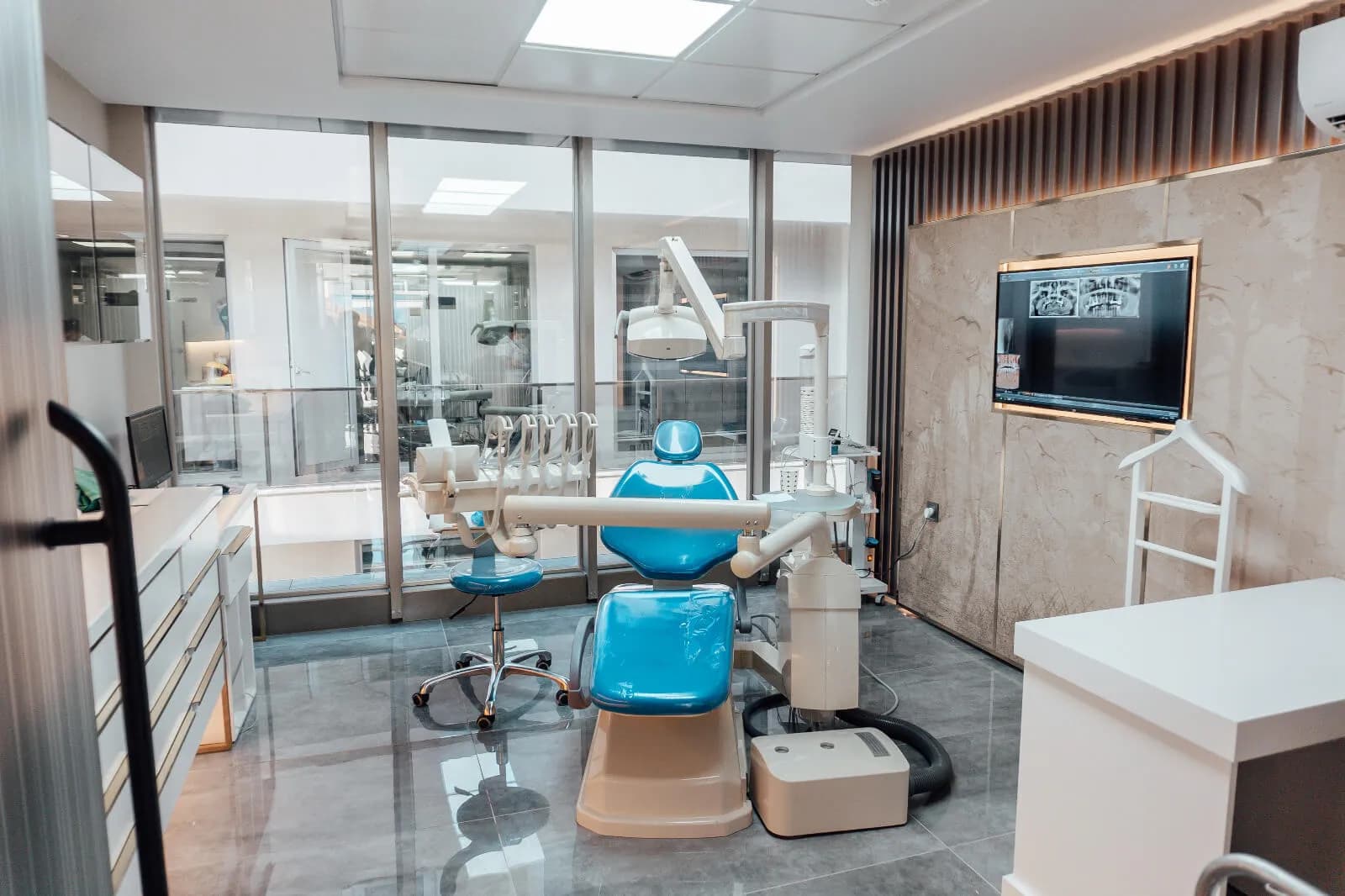 Ein Behandlungsraum von Ballıpınar Dental mit Behandlungsstuhl, OP-Leuchte und einem Bildschirm mit Panoramaröntgenaufnahmen