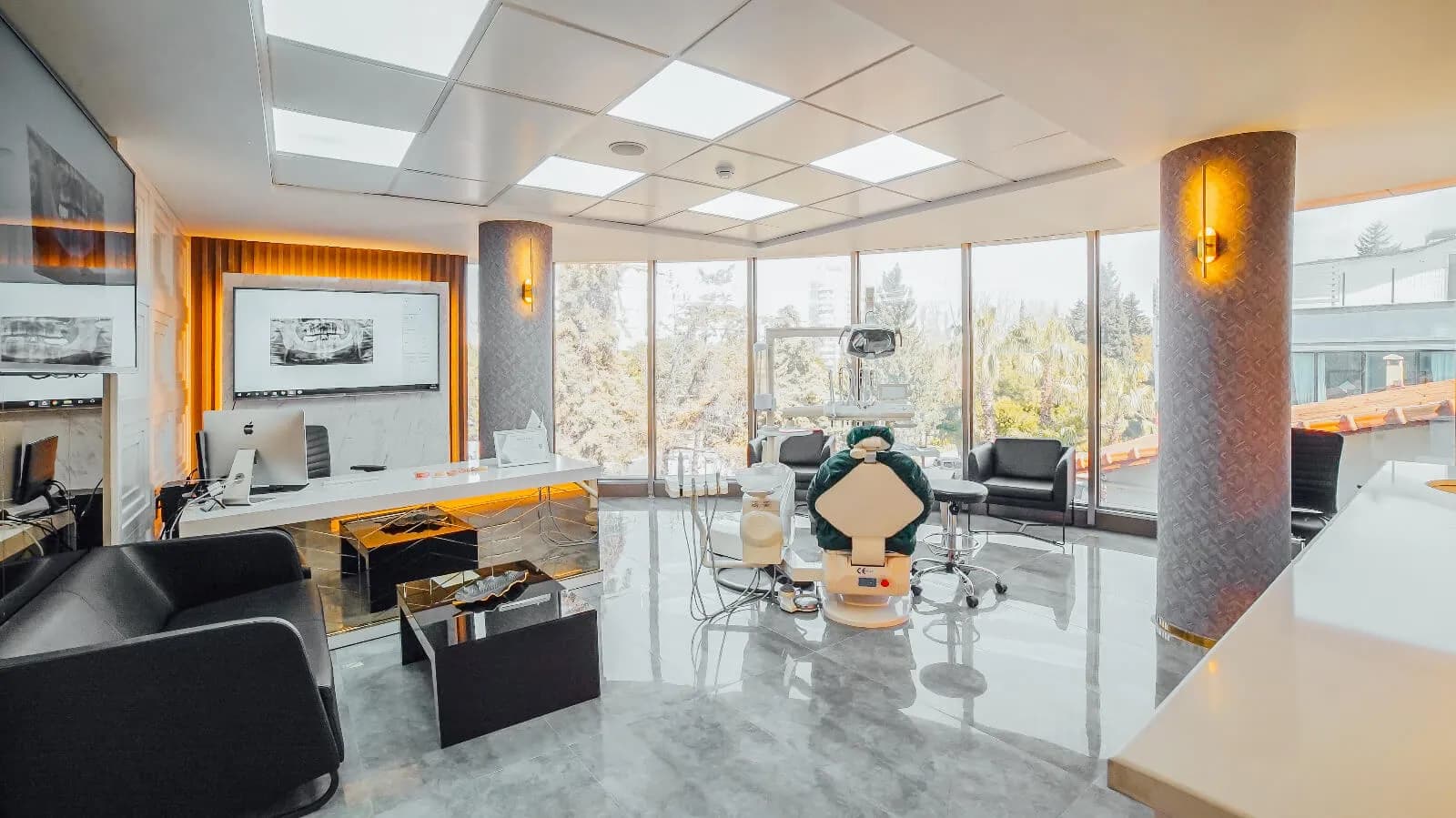 Ein Eck-Behandlungsraum von Ballıpınar Dental mit raumhohen Fenstern auf zwei Seiten und Röntgenbildern auf einem Wandbildschirm