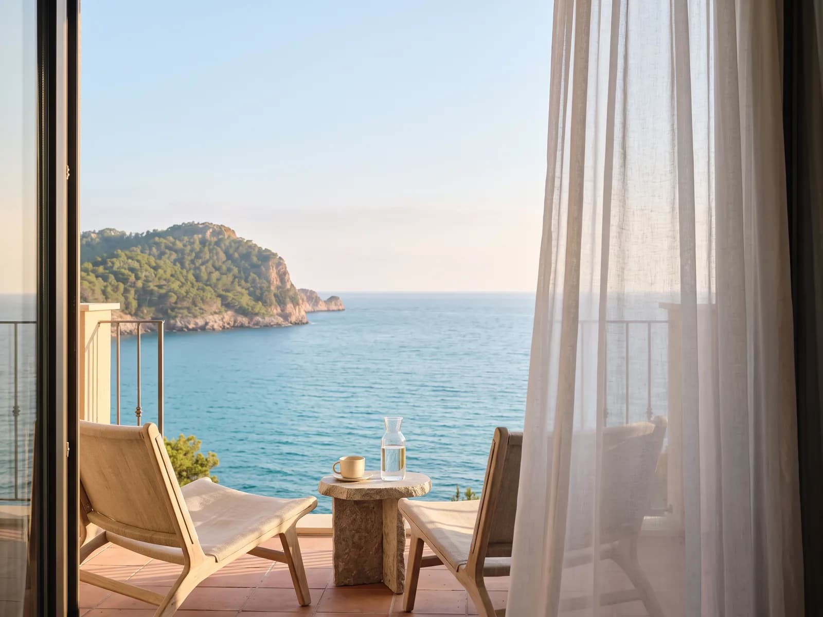 Der Balkon desselben Hotelzimmers, zwei niedrige Sessel und ein Steintisch mit Blick aufs Meer
